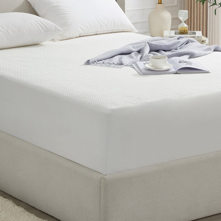 Bed with white mattress cover and beige bed frame in a bedroom setting.