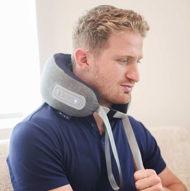 Man wearing a neck massager device on a neutral background