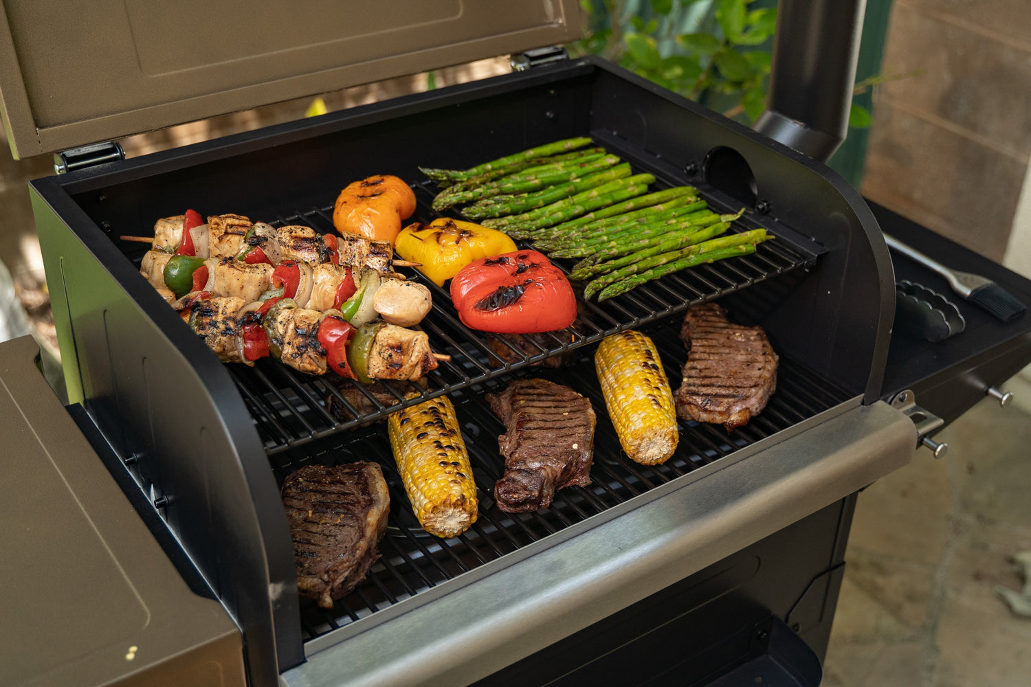 Grill with various foods cooking on it, including vegetables and meats.