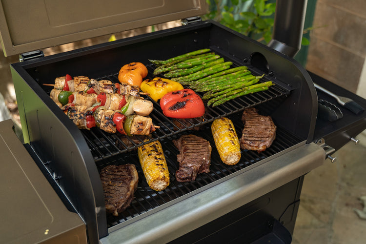 Grill with various foods cooking on it, including vegetables and meats.