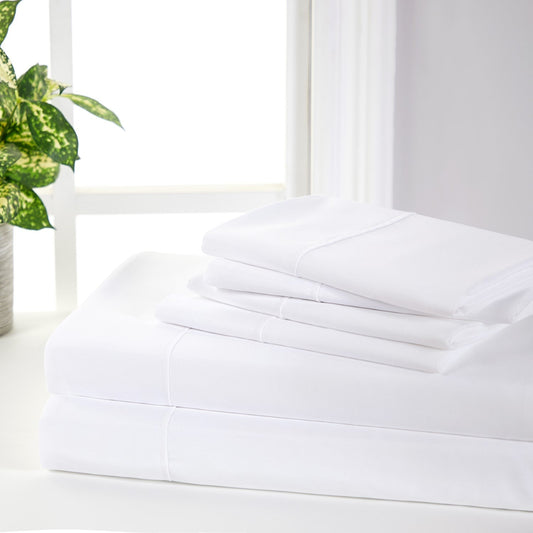 A white 6-piece bamboo sheet set on a bed, including a fitted sheet, flat sheet, and pillowcases, presented in a bright room setting with decorative plants and a nightstand.