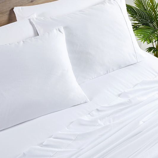 A white 6-piece bamboo sheet set on a bed, including a fitted sheet, flat sheet, and pillowcases, presented in a bright room setting with decorative plants and a nightstand.