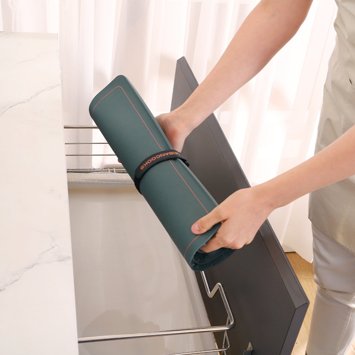 Person holding a green yoga mat with a red border against a white curtain background