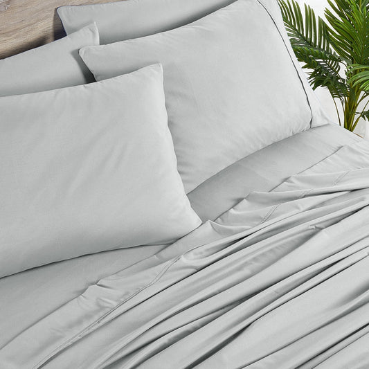 A silver 6-piece bamboo sheet set on a bed, including a fitted sheet, a flat sheet, and pillowcases, presented in a well-lit room with a plant and nightstand beside the bed.