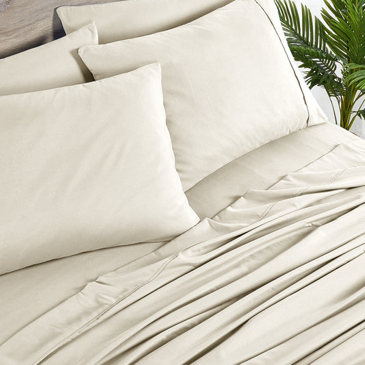 A cream-colored bamboo sheet set on a bed, including a fitted sheet, flat sheet, and pillowcases, with a wooden headboard and houseplants in the room.