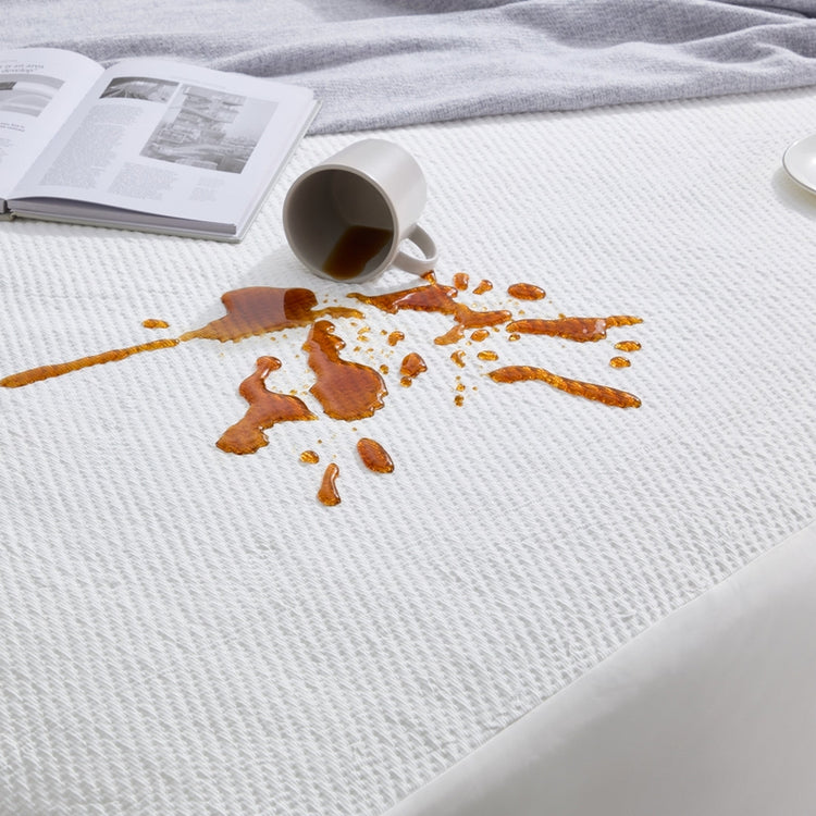 Mattress with coffee spill and cup on top, next to a book.