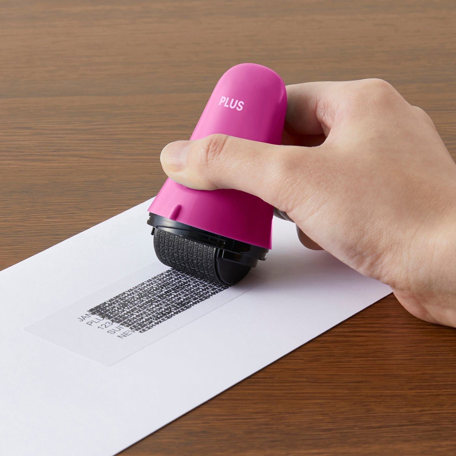 Hand using a pink roller tool on a piece of paper with text, on a wooden surface.
