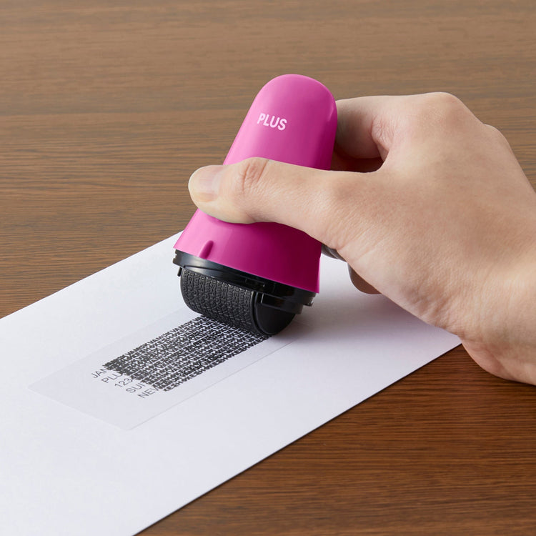 Hand using a pink roller tool on a piece of paper with text, on a wooden surface.
