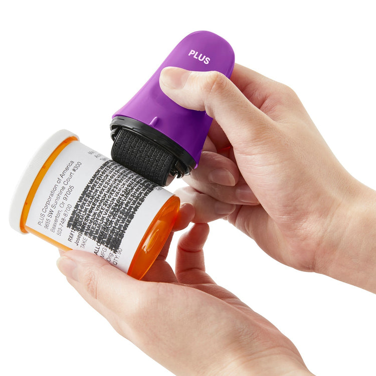 Hand using a purple labeler to apply a label to a prescription bottle on a white background