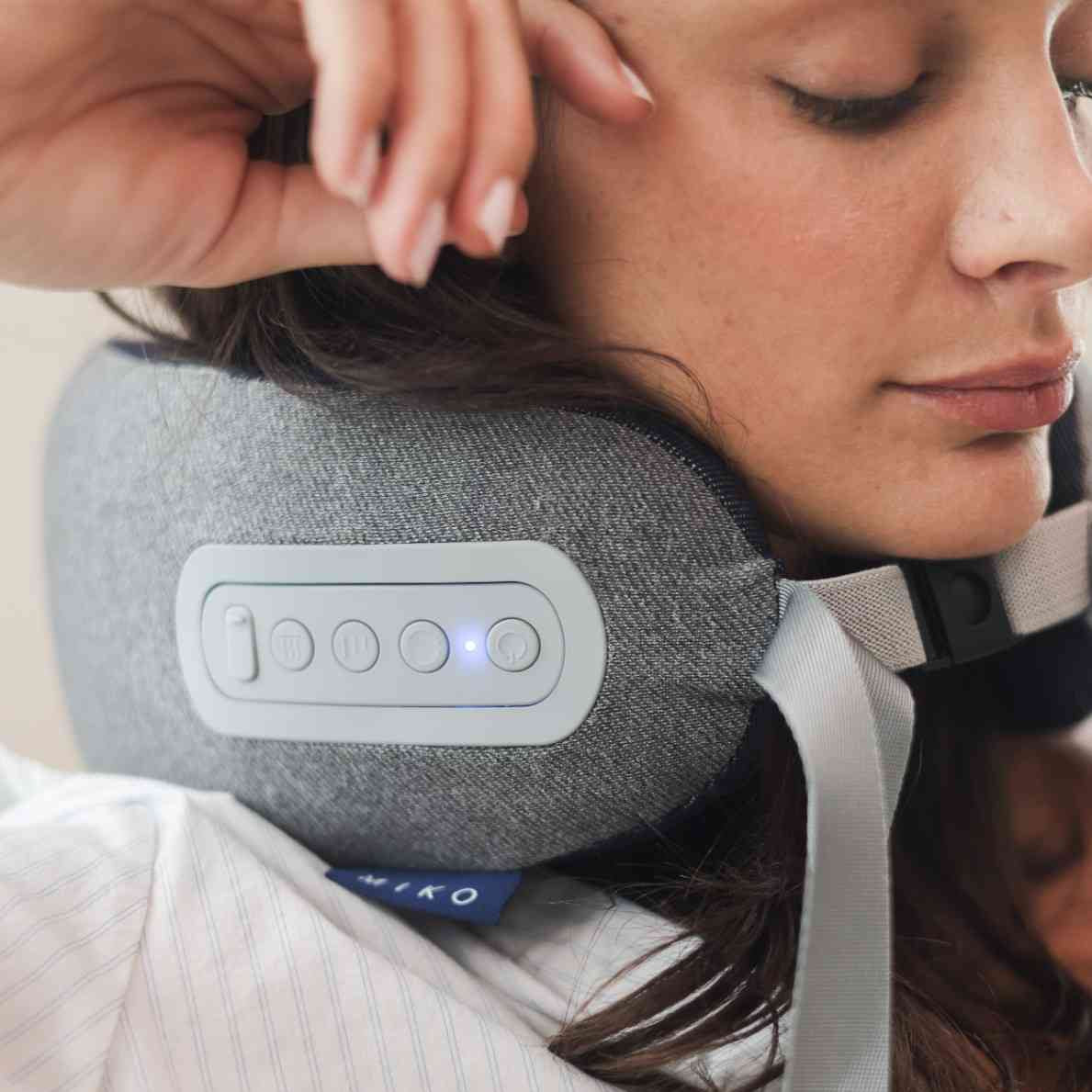 Woman using a gray neck pillow with control panel, brand 'MIKO' visible
