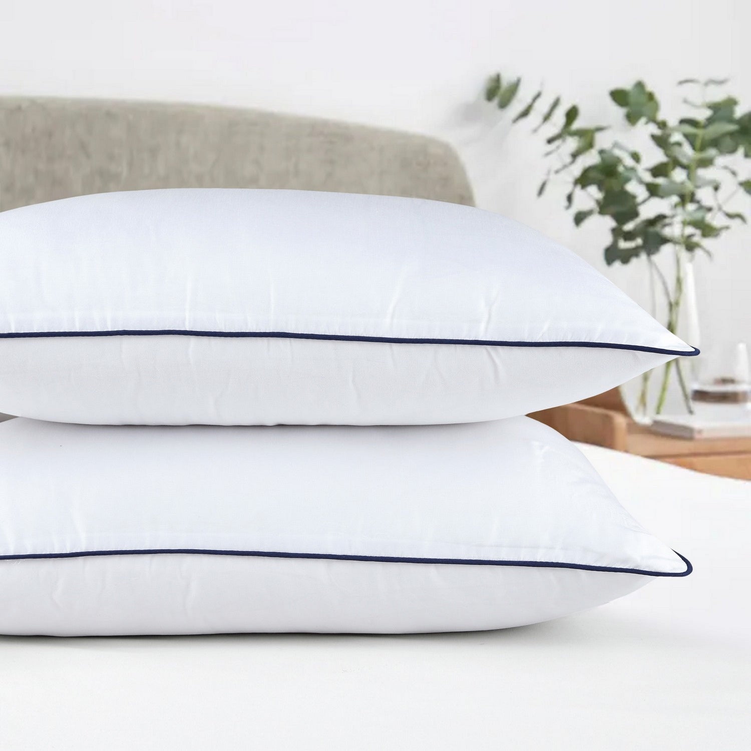 Two white pillows with a blue stripe on a light surface, with a blurred background of a room.