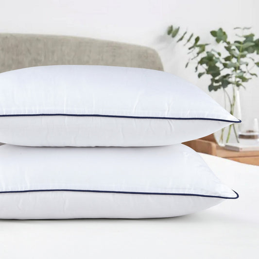 Two white pillows with black piping on a white background