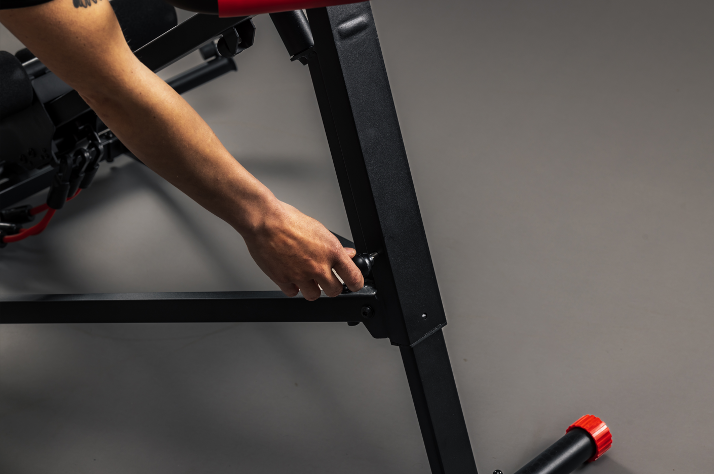 Person adjusting a piece of gym equipment on a gray floor.