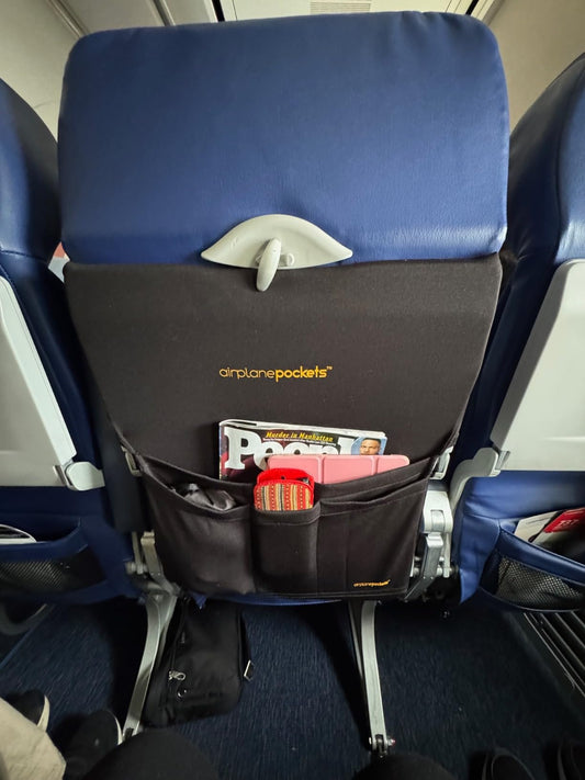 Airplane seat with a pocket organizer containing snacks and a magazine.