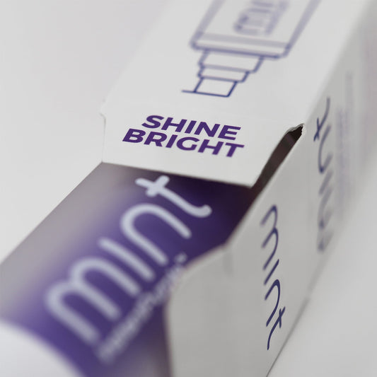 A product image showing a box and tube of Mint InstantPurple Color Corrector with nHAp. The packaging is primarily purple and white with text detailing the product's benefits and instructions for use.