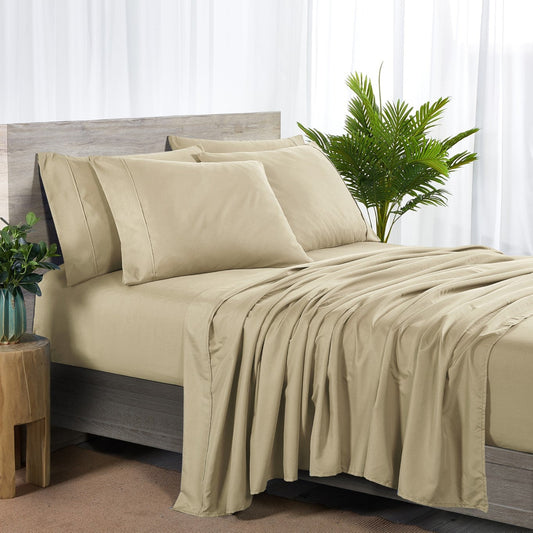 A warm taupe colored 6-piece bamboo sheet set on a bed, with a flat sheet, fitted sheet, and pillowcases displayed. The bed is set against a room backdrop with a plant and nightstand on the side.
