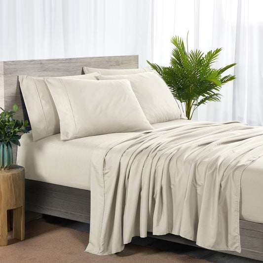 A cream-colored bamboo sheet set on a bed, including a fitted sheet, flat sheet, and pillowcases, with a wooden headboard and houseplants in the room.