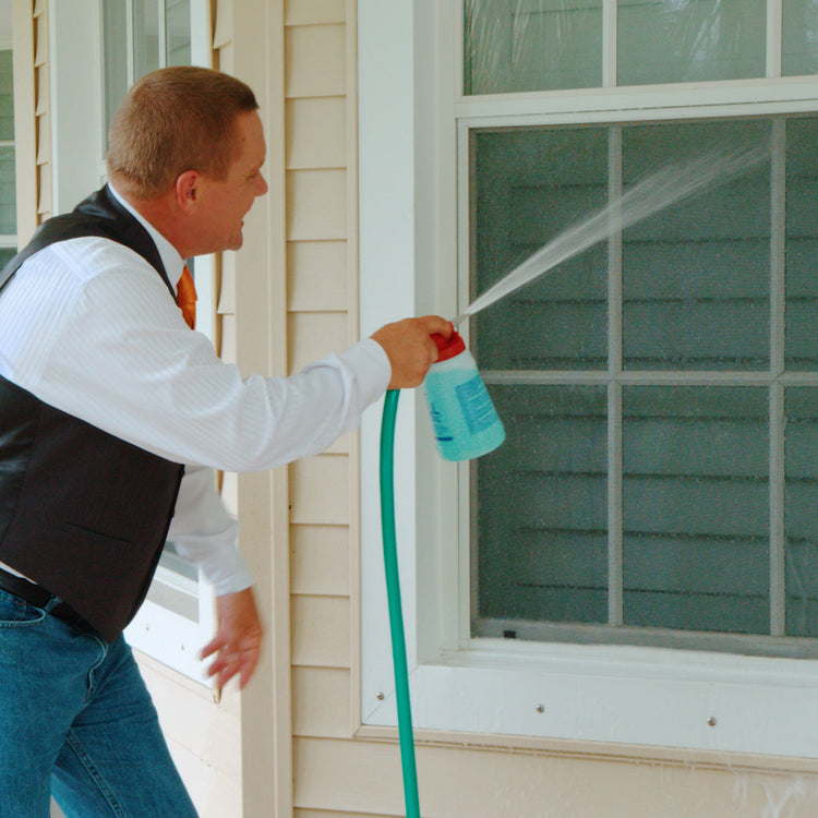 Man using a spray bottle and hose outside a house