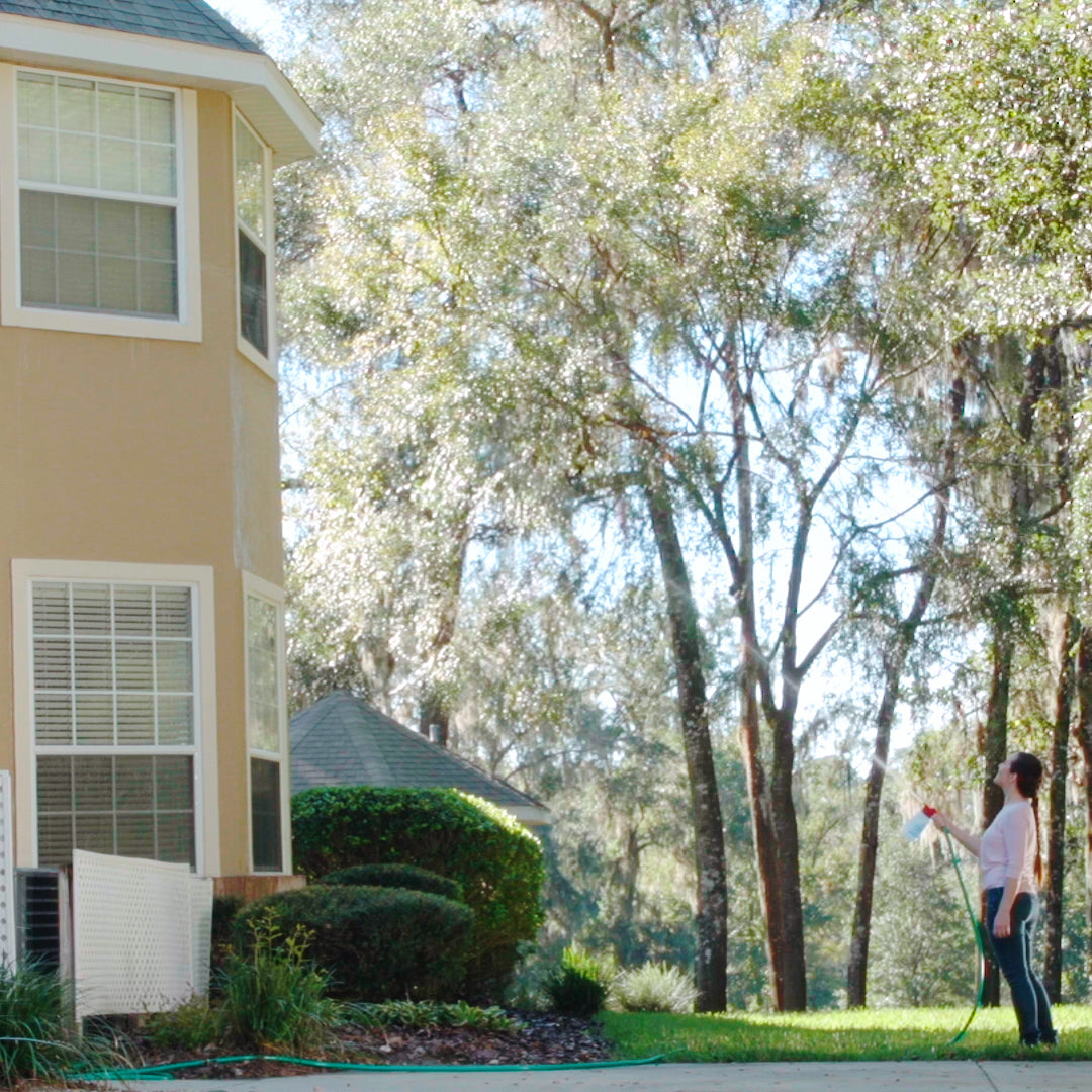 Woman using a pressure washer in front of a house with trees in the background