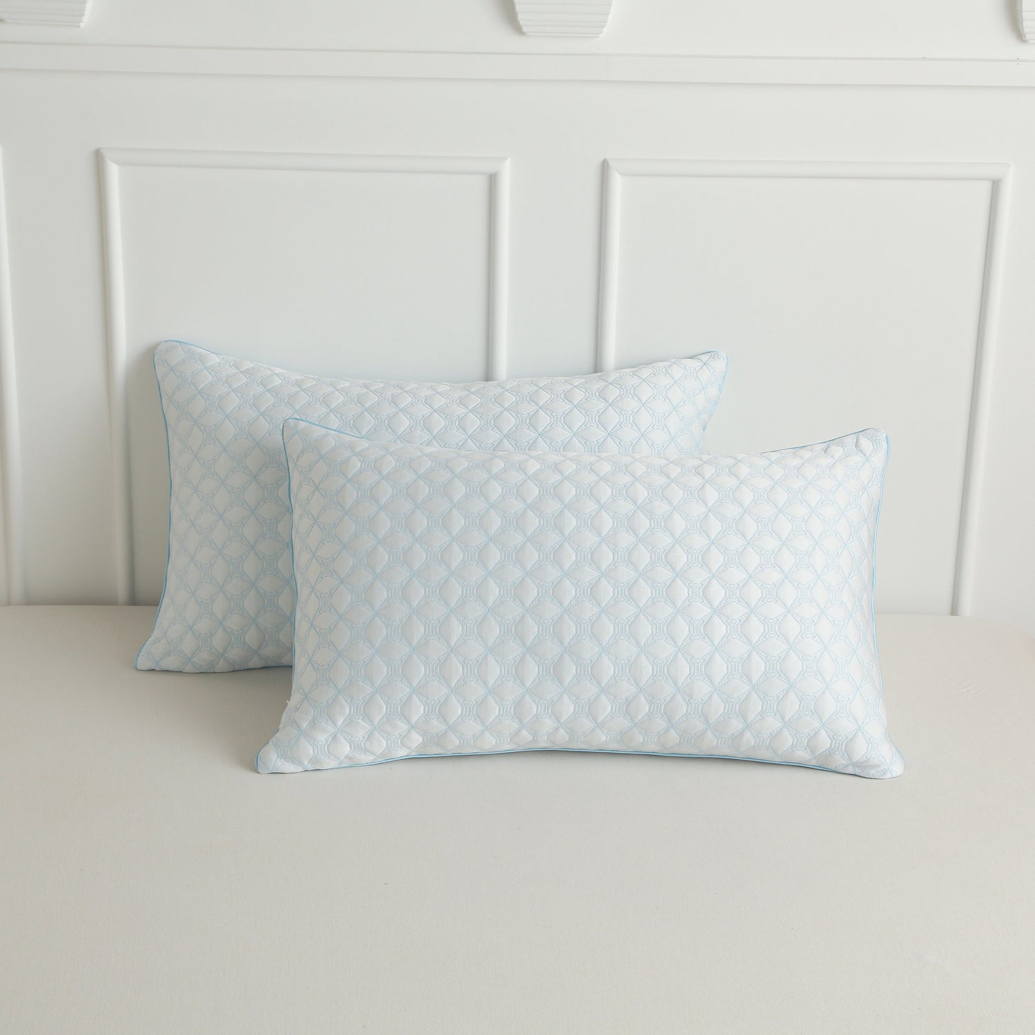 Two light blue patterned pillows on a bed with a white headboard.