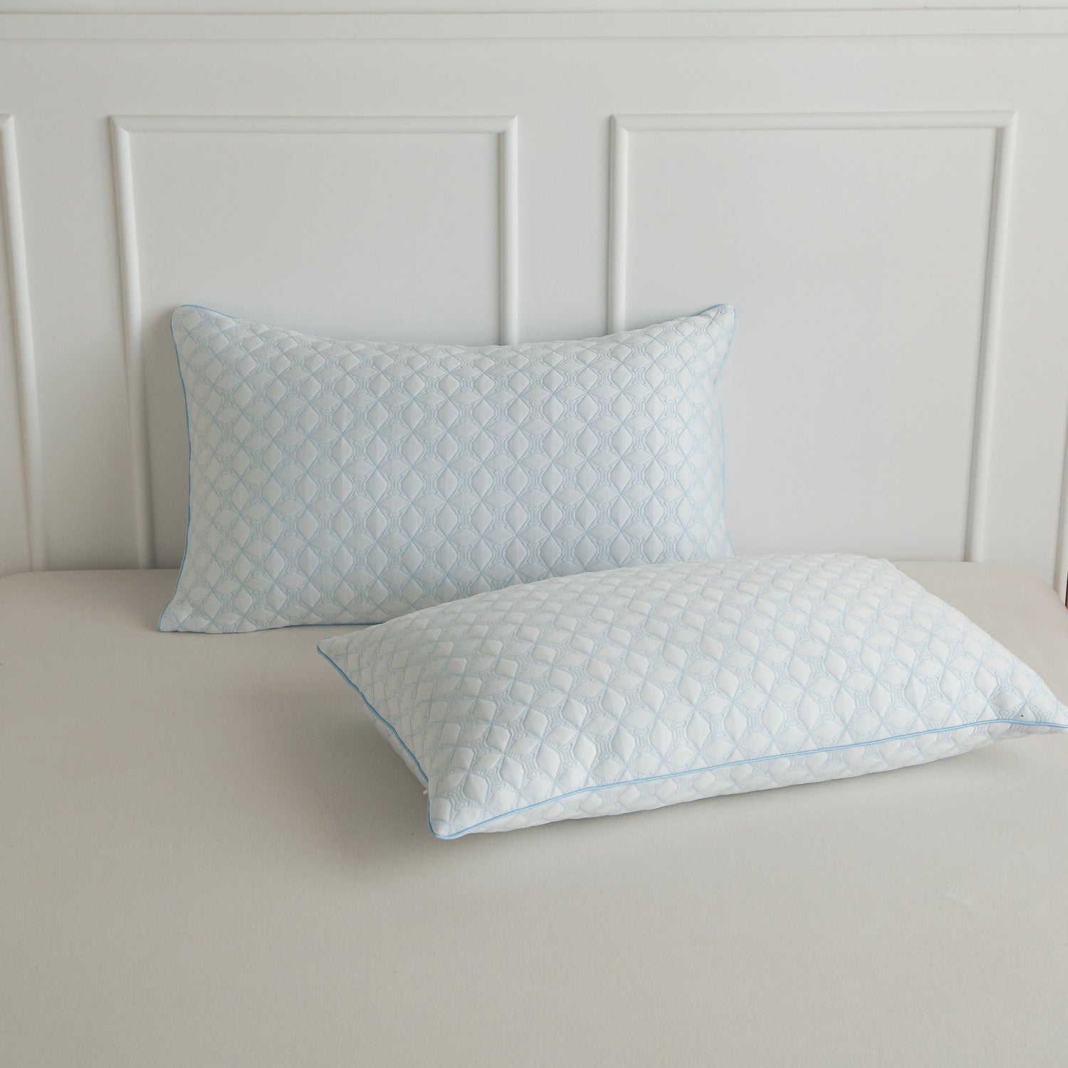Two quilted pillows on a bed with a neutral headboard.